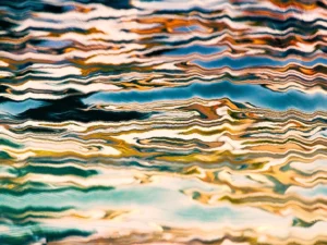 Rippled layers of teal, gold, and cream flows, creating a fluid abstract with dynamic movement.