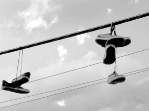 Hanging sneakers silhouetted against cloudy sky, suspended from overhead power lines.