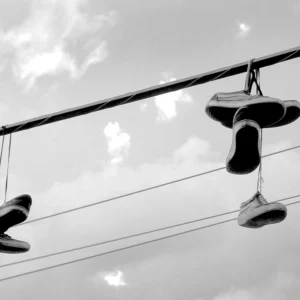Hanging sneakers silhouetted against cloudy sky, suspended from overhead power lines.