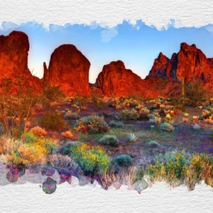 Fiery red rock formations rise above vibrant desert flora in fading sunlight.