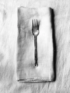 Vintage fork rests on folded linen napkin, textured fabric softly illuminated.
