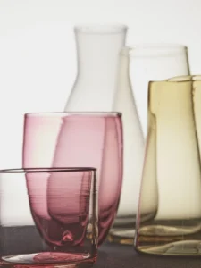 Soft light dances through tinted glass vessels, revealing delicate hues and graceful curves.