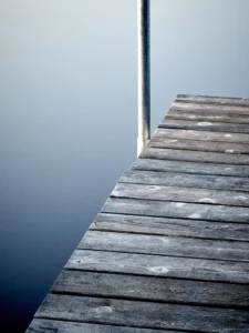 Weathered wooden dock meets still blue water, capturing tranquility in minimalist harmony.