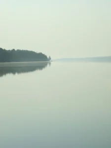 Misty horizon stretches endlessly, still water mirrors tranquil pale morning light.