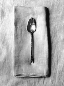 Vintage spoon rests gracefully atop textured linen, simple elegance in monochrome.