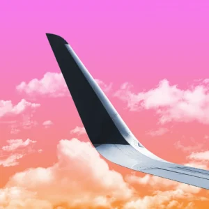 The upturned wing of a plane passes through a candy colored sky.