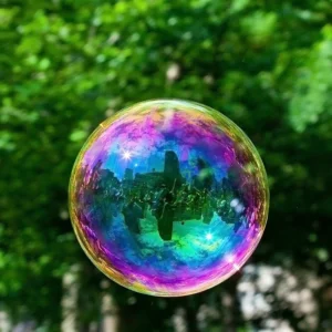 The artist can be seen in a crowd within the iridescent bubble, a moment suspended in time and space.