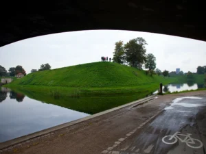 Snapshot from under a bridge on the bike lane at a scenic park. A group of people can be seen spectating across the waterway on a grassy knoll.