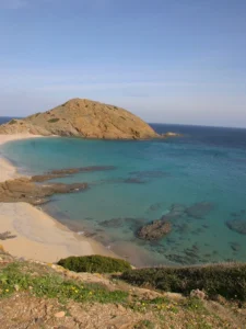 A serene turquoise beach, protected by a shell-shaped cove and rocky scenery.
