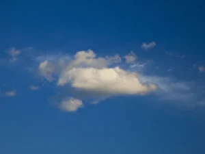 Within a vast blue sky floats a fluffy cumulus cloud, forever preserved in photo.