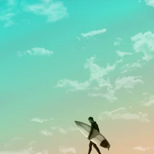 A lone surfer, carrying their longboard, strolls beneath a pale, gradient sky.