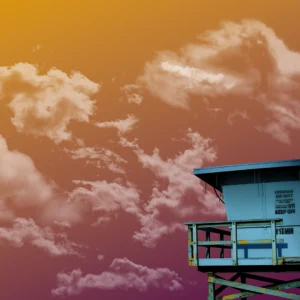 An abandoned lifeguard tower peaks into view under a peachy, golden sky.