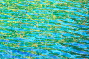 Glimmers of green and yellow shine on the surface of a rippling pool of blue water.
